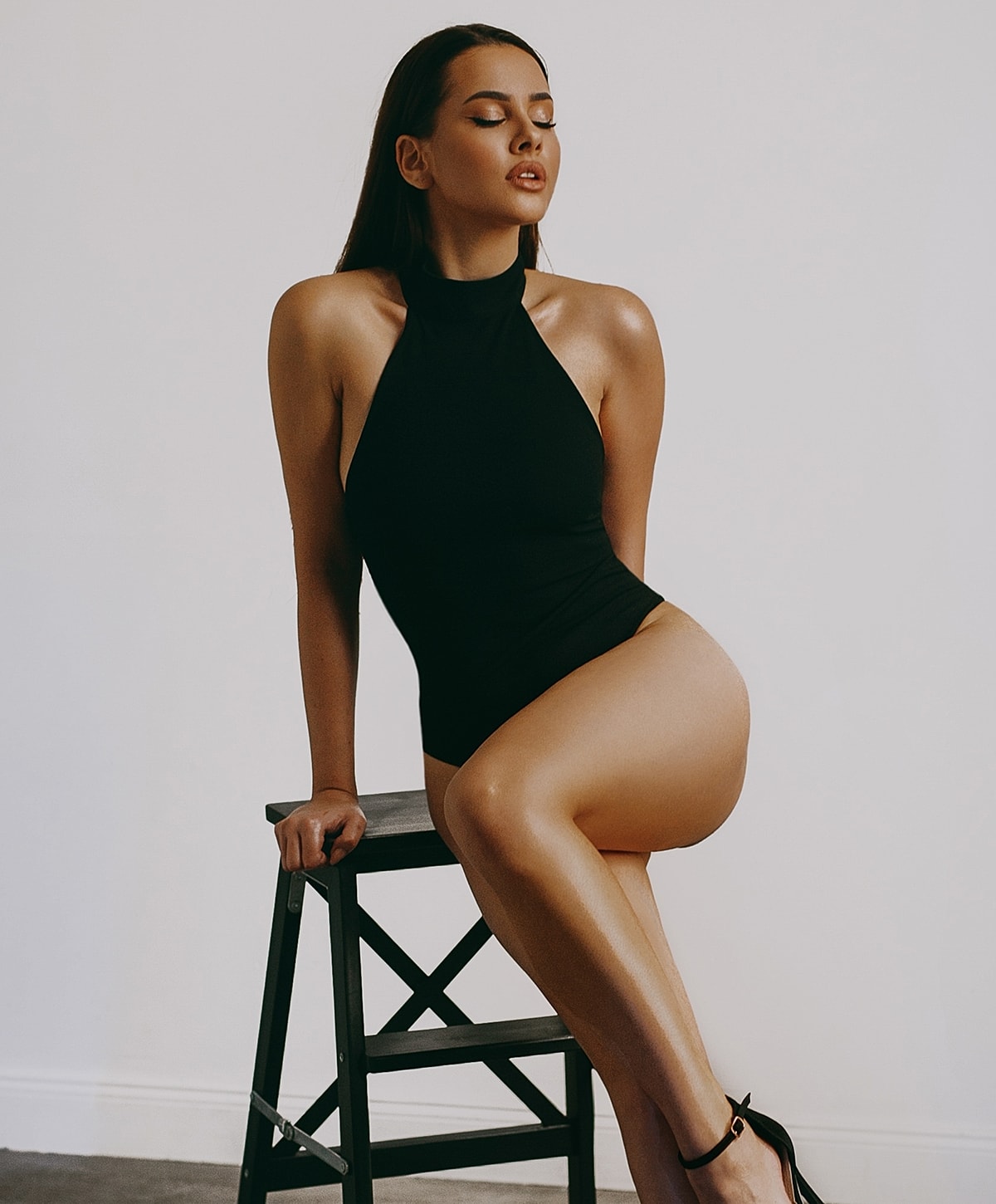 Model seated on stool in stylish black outfit.