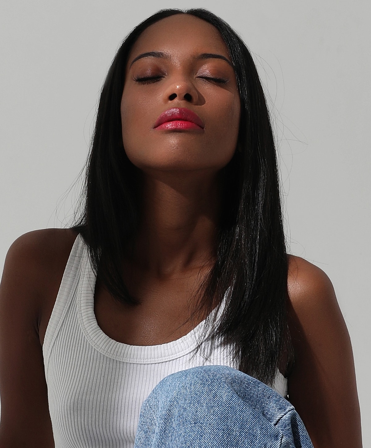 Woman with closed eyes, wearing a white tank top.