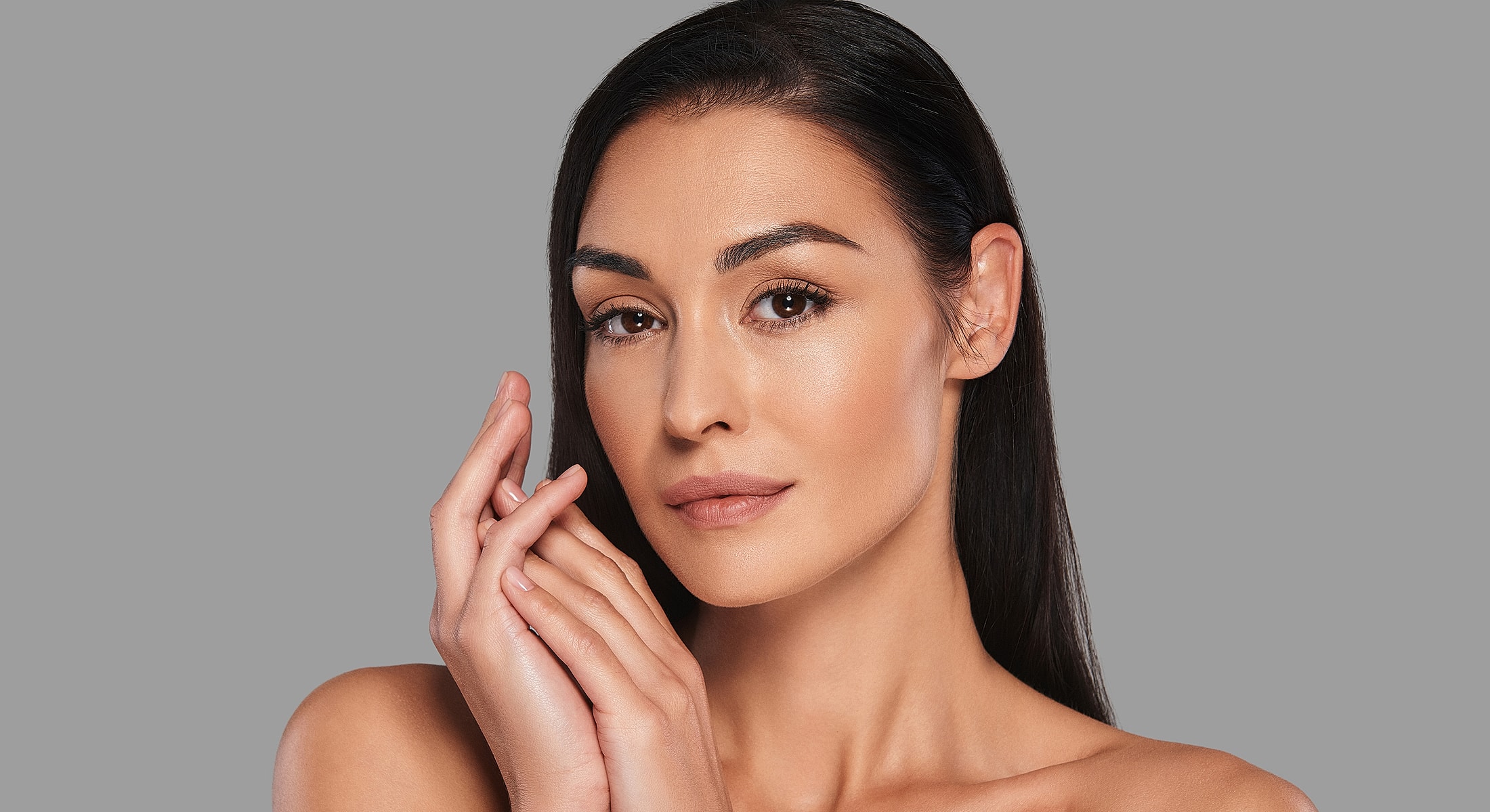 Woman touching her face with a neutral background.